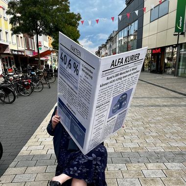 Frau mit übergroßer Zeitung sitz in der Fußgängerzone